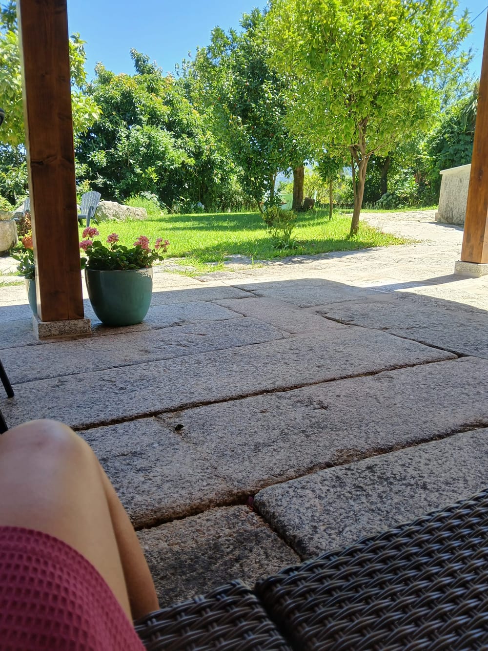 O alpendre sobre o jardim, com o lajedo em granito e as arvores em frente.