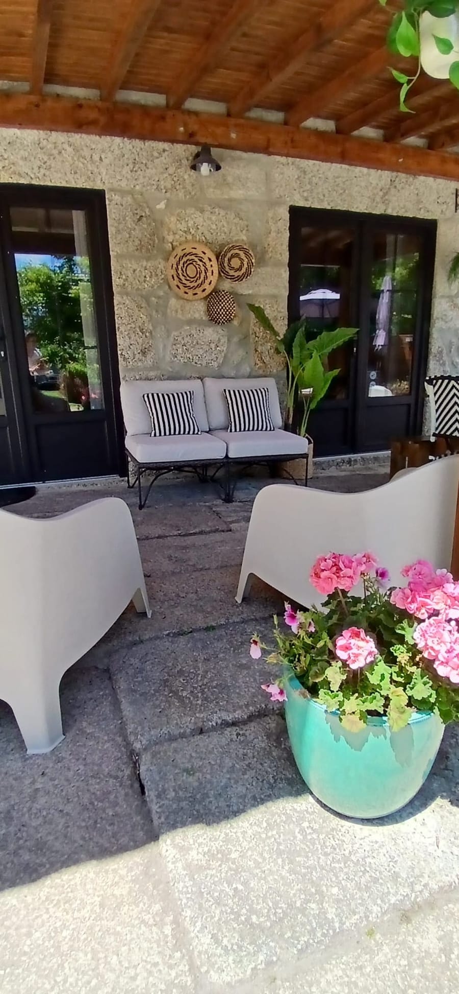 O alpendre, com o teto em madeira, os sofas e um vaso de sardinheiras.