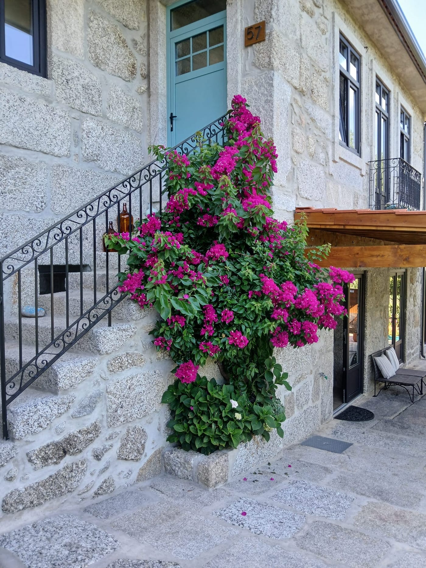 A escada em granito e a porta azul, com a buganvilia em flor.