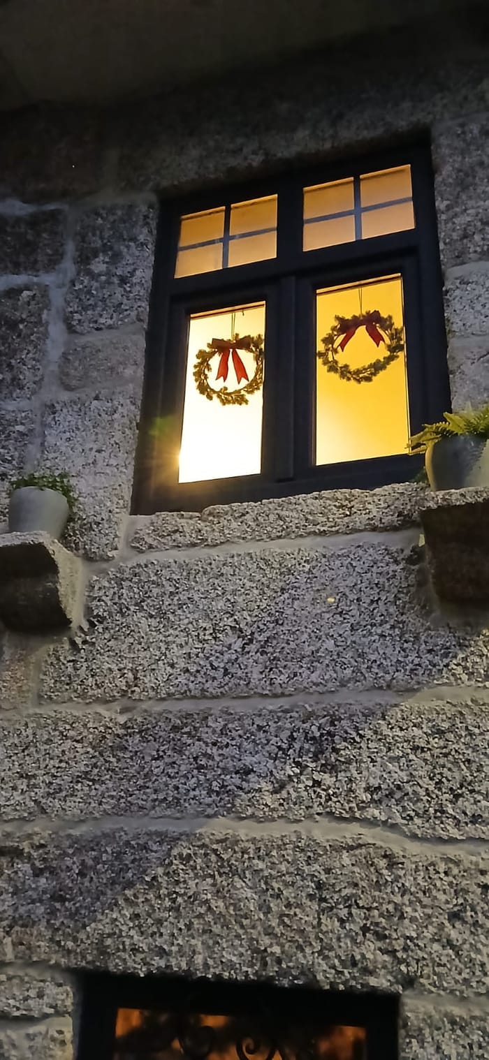 A janela em granito iluminada, com duas coroas de Natal, ao anoitecer.