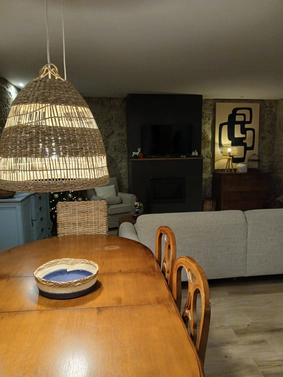 A sala de jantar, com a mesa em madeira e o candeeiro de vime suspenso.