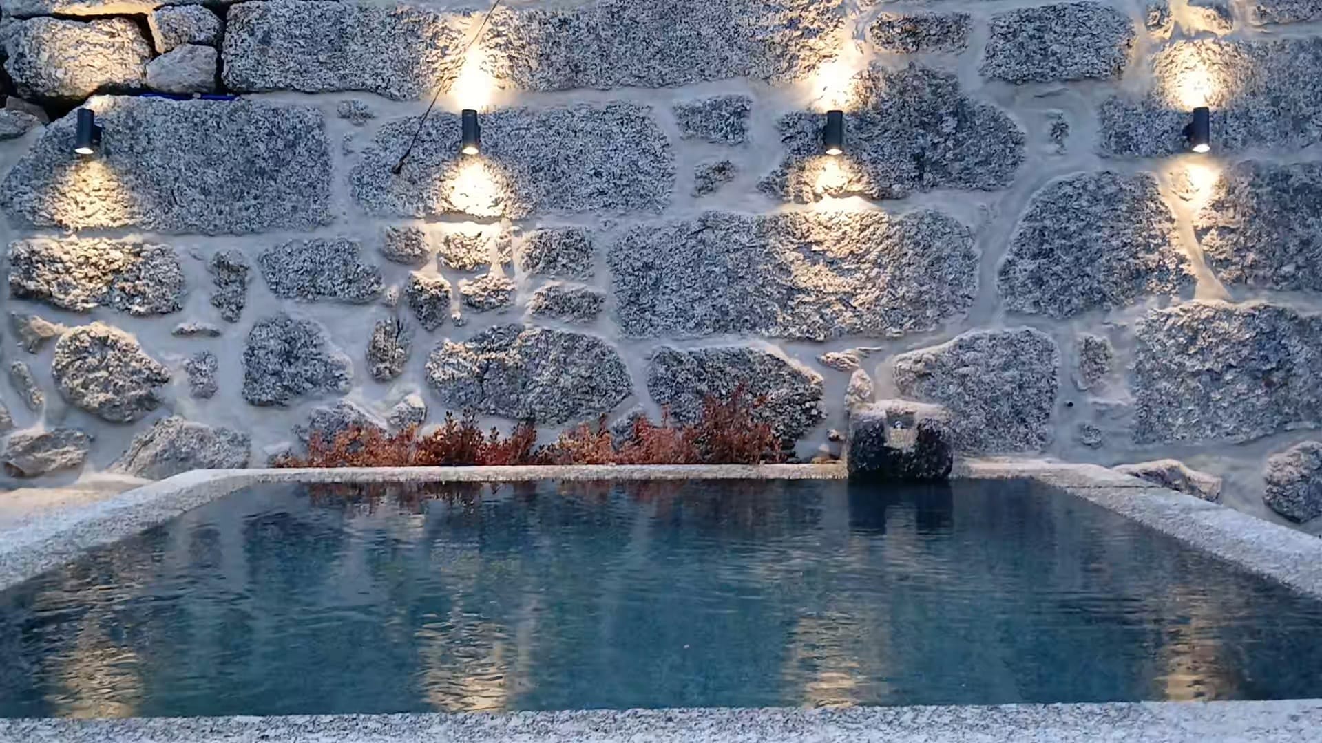 O tanque de granito ao anoitecer, as luzes de parede refletidas na agua.